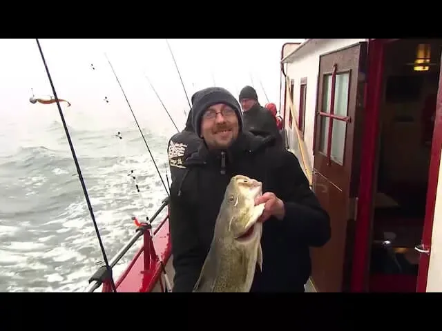 Angler mit einem gefangenen Dorsch an Bord eines Fischkutters