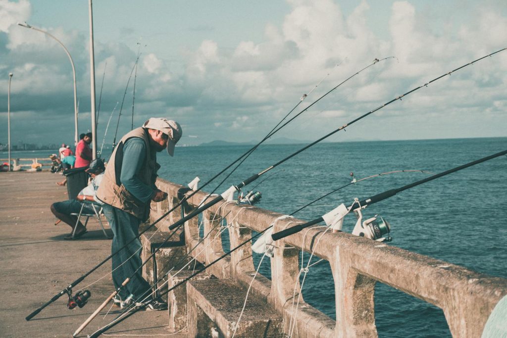 A group of fishermen enjoy a sunny day by the sea, casting lines from a pier.